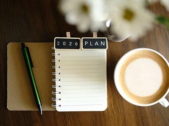 notebook with tabs saying 2026 plan at the top, next to pen, coffee cup and flowers